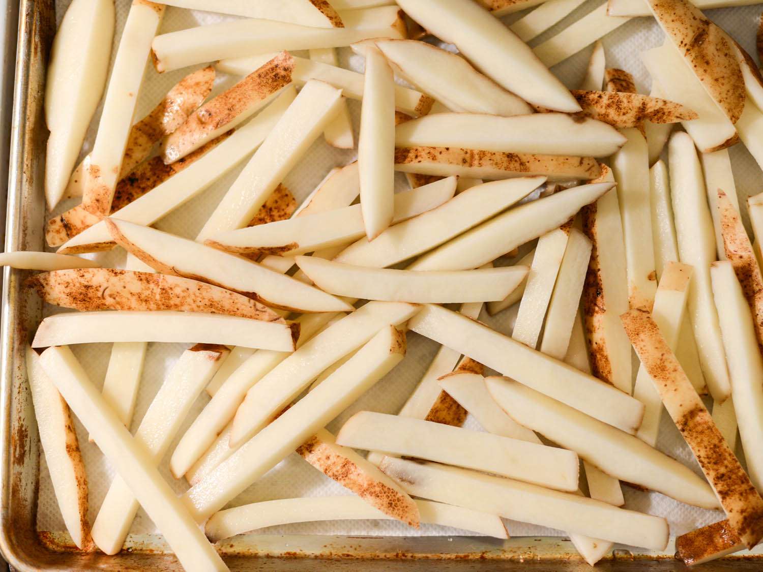 Fresh cut potato fries laid out on rimmed baking sheet.