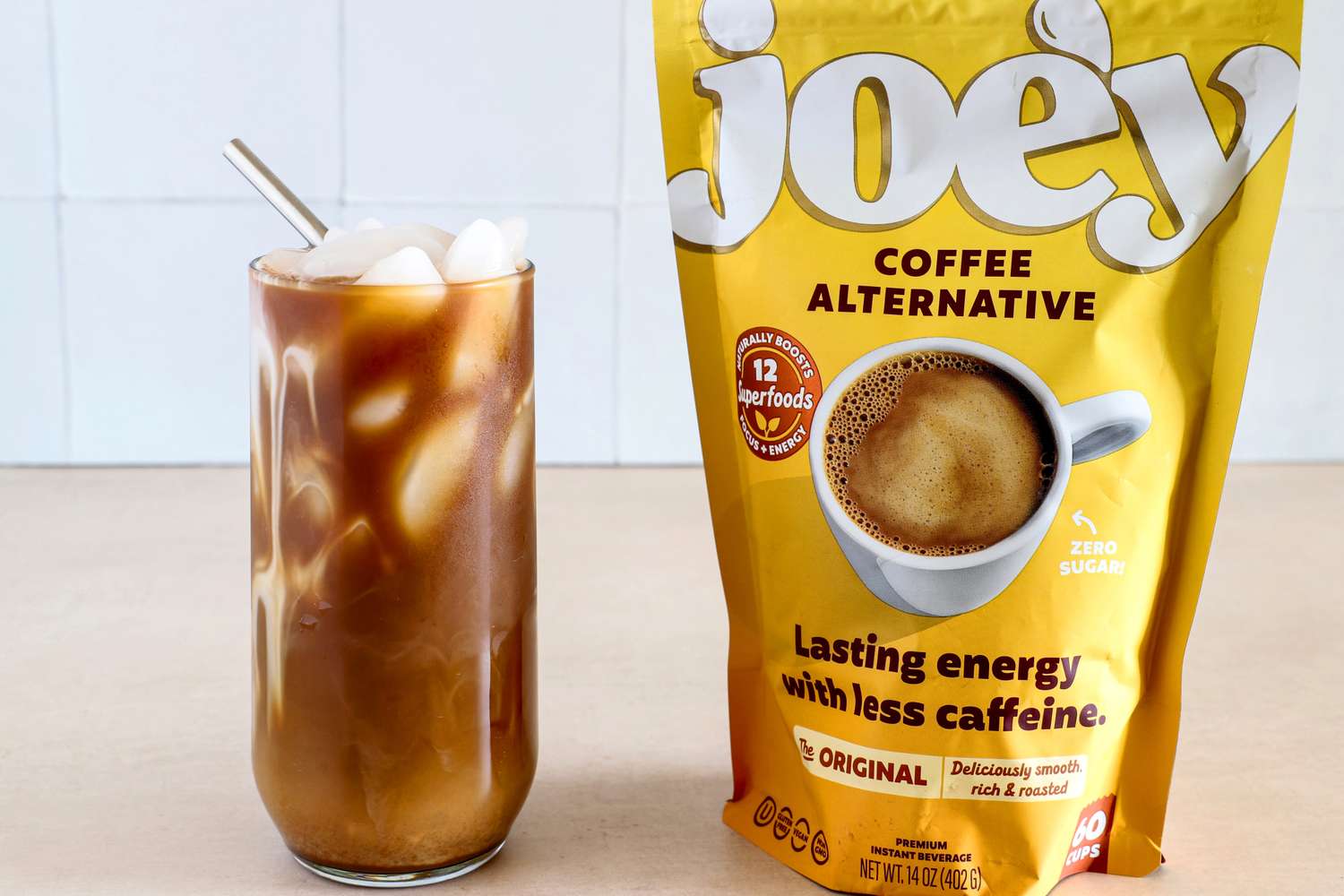 A glass of iced coffee drink next to a package of Joe'y coffee alternative granules on a table