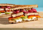 A marinated tofu sandwich layered with vegetables and spread on whole grain bread