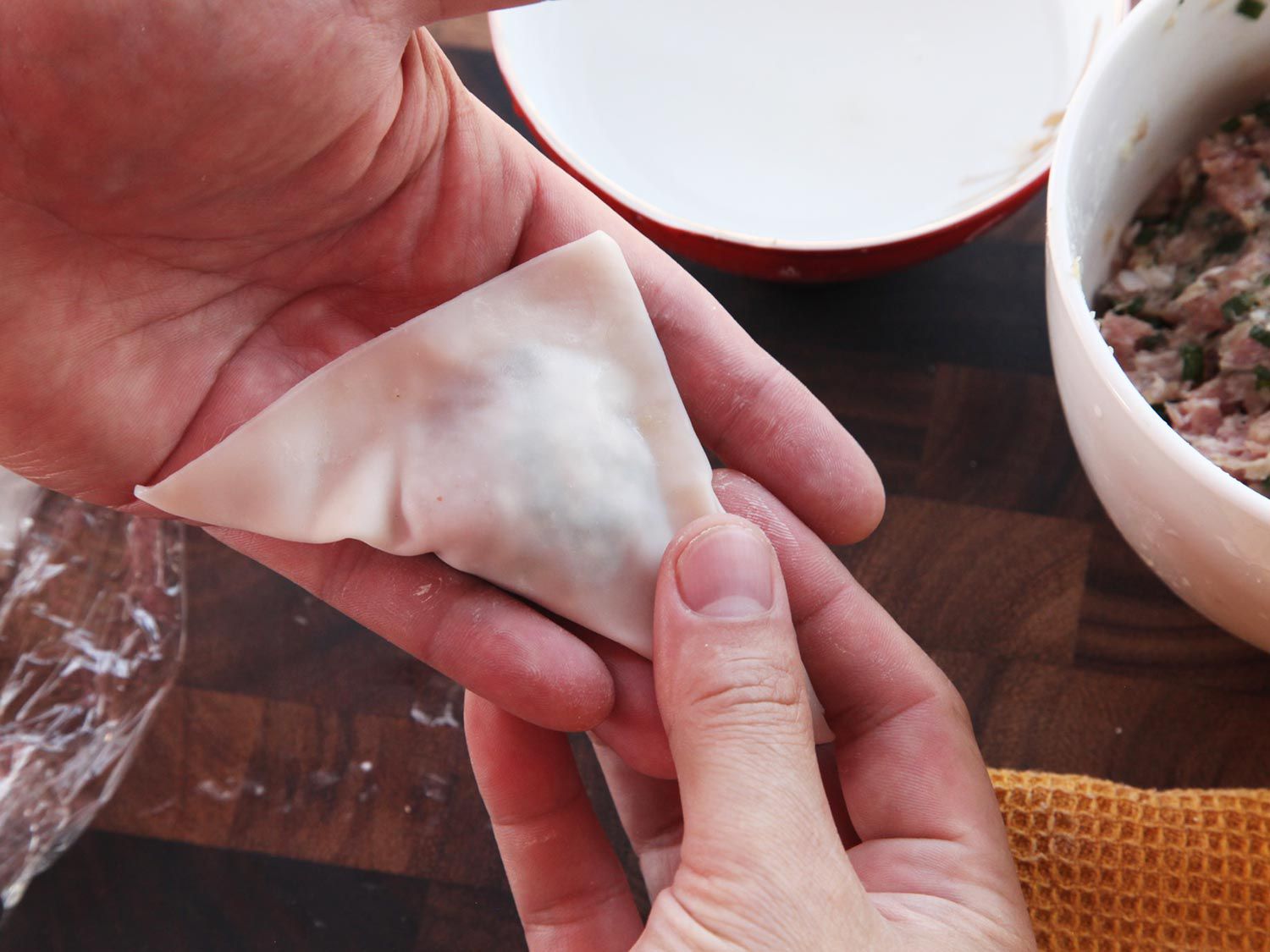 Folding over wonton wrapper to form triangle and sealing edges
