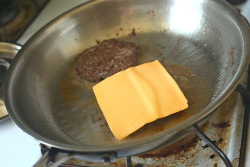 The patties for a better Big Mac are panfried on their second side. A slice of American cheese has been draped over one of the patties.