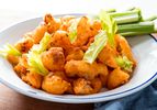 A plate of crispy buffalo fried cauliflower, with celery sticks on the side of the plate.