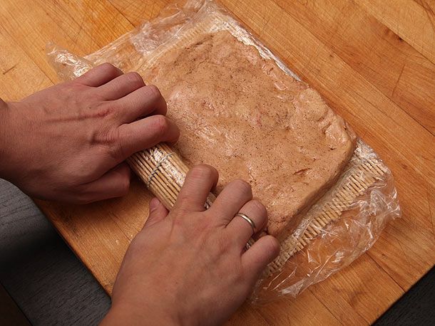 Author rolling the square of foie gras into a cylindrical shape using a sushi-rolling mat.