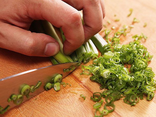 The final part of a process showing how to pull a knife backward to slice scallions.