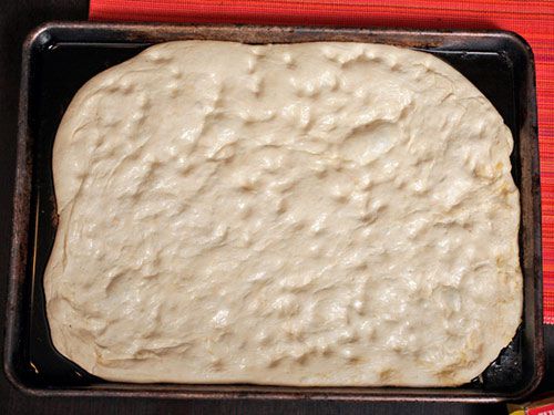 Overhead view of pizza bianca dough that has been stretched out and left to rise in a sheet pan. The dough rests directly on the oiled surface of the pan.