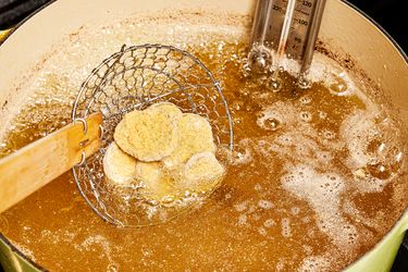 Dipping breaded pickles into heated oil in dutch oven with slotted spoon 
