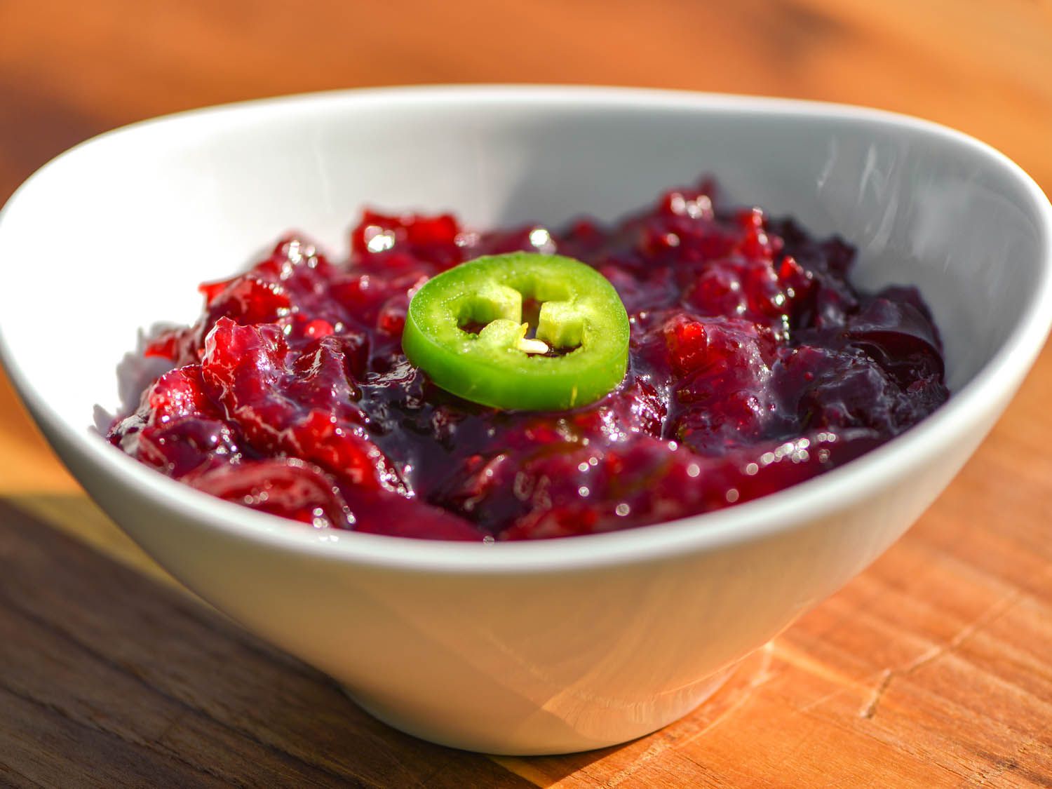 A bowl of cranberry sauce, garnished with a slice of jalapeno. 