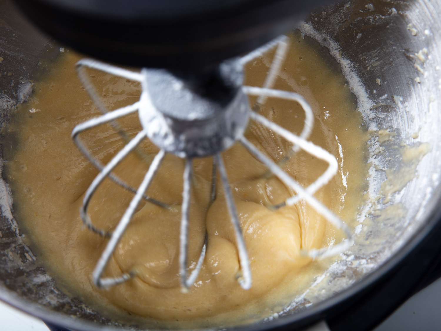 Adding flour to a stand mixer bowl filled with batter for French apple cake.
