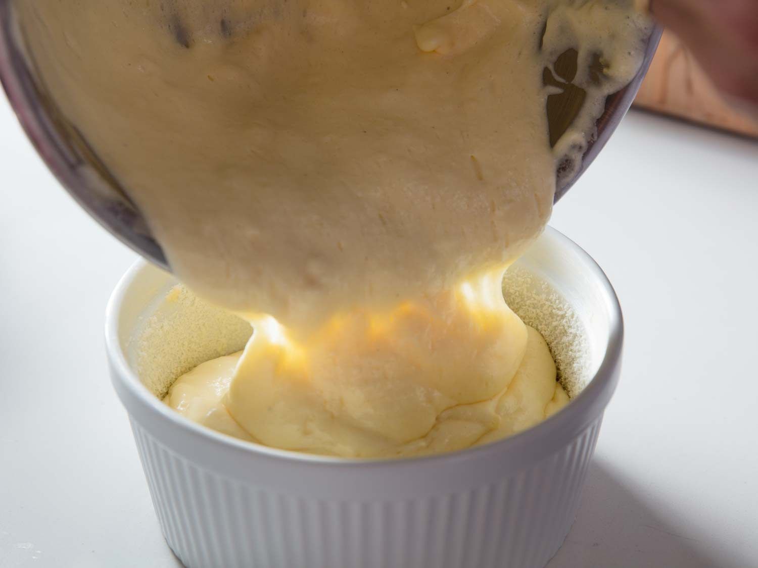 Pouring soufflé batter into the prepared baking dish from a bowl.