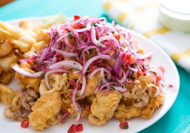 A pile of fried mixed seafood topped with lime-marinated red onions, tomatoes, and cilantro