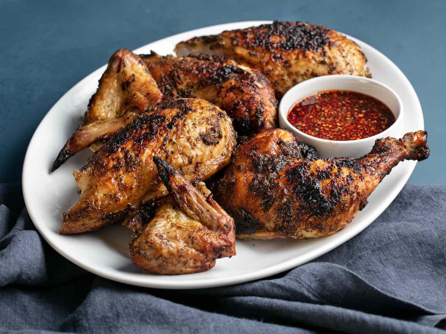 Thai-style grilled chicken on a platter with sauce.