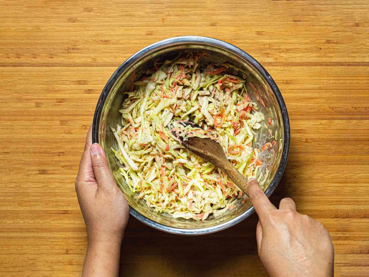 Overhead view of mixing shredded vegetables with dressing