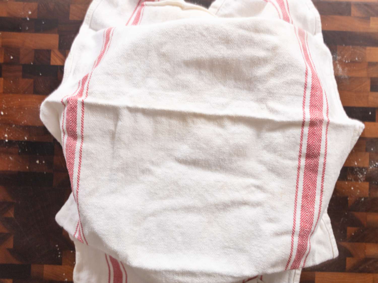 Bowl covered in white kitchen towel on a wooden chopping block
