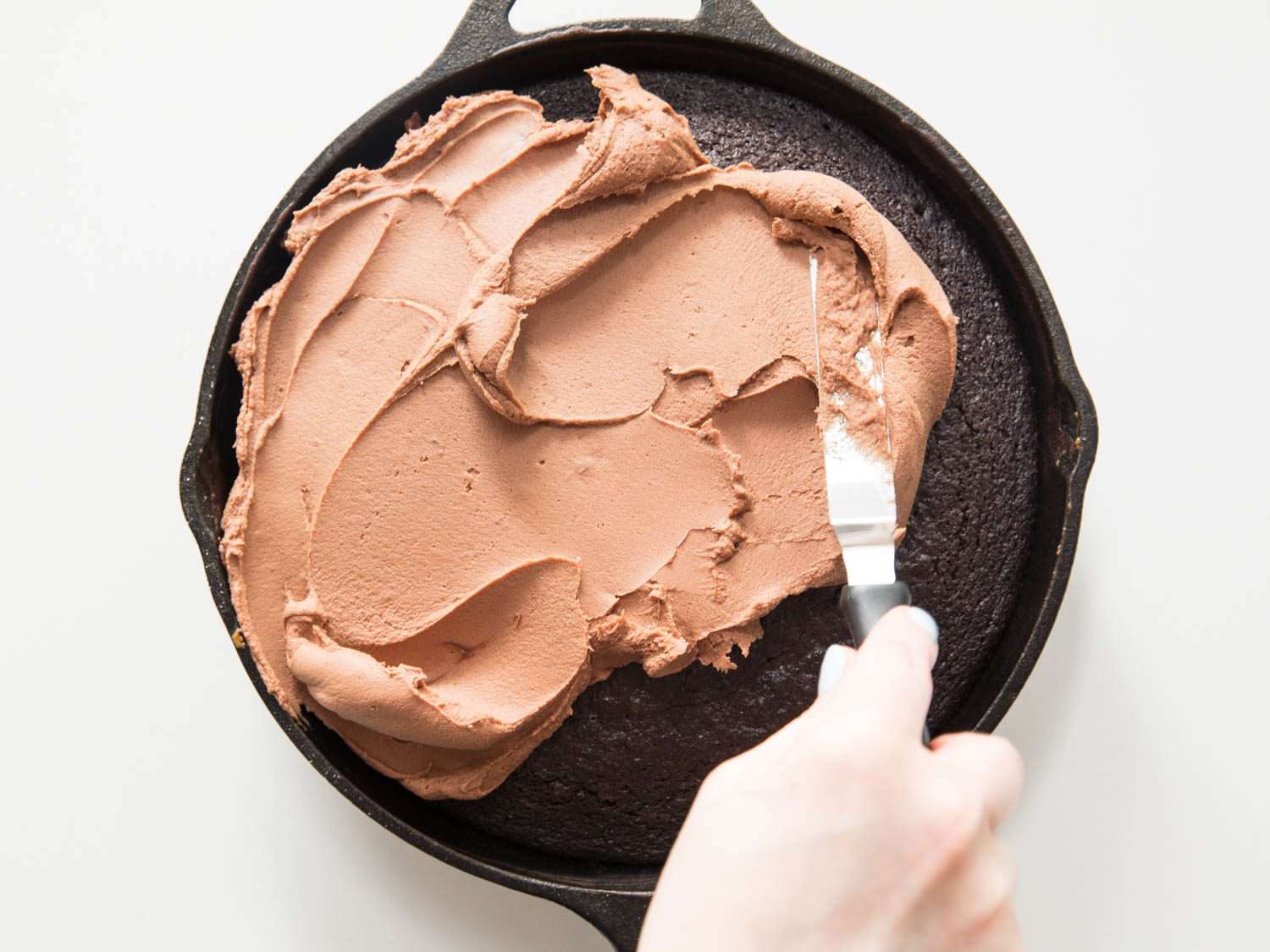 Overhead shot of milk-chocolate ganache frosting being spread over a chocolate skillet cake.