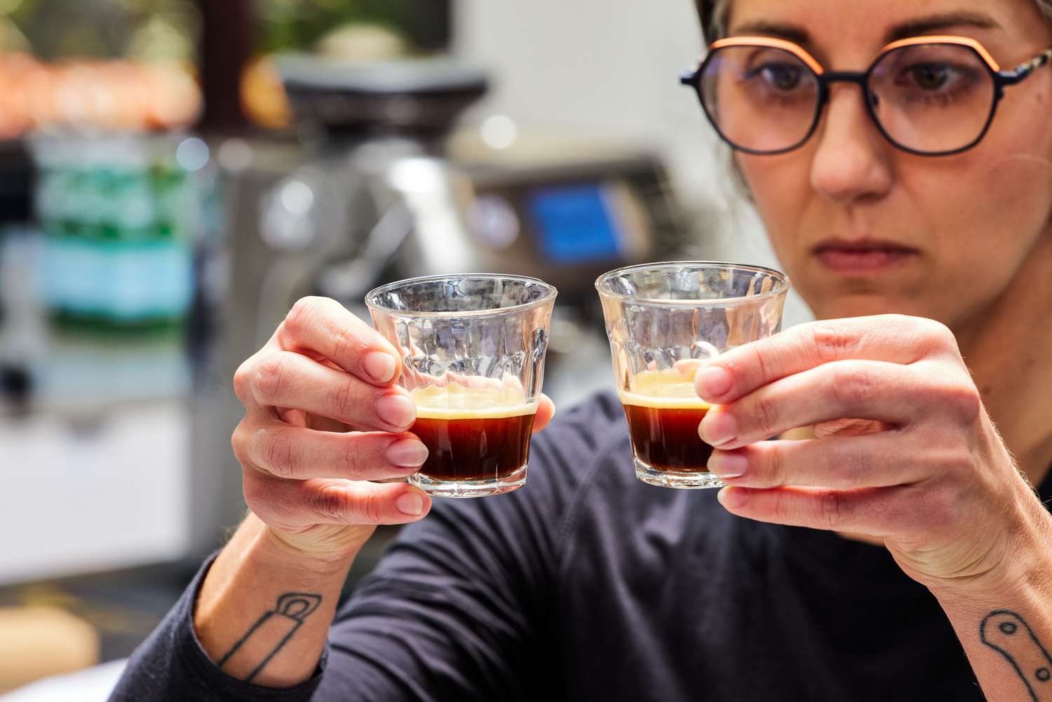 A person holding up two glass espresso cups with espresso inside 