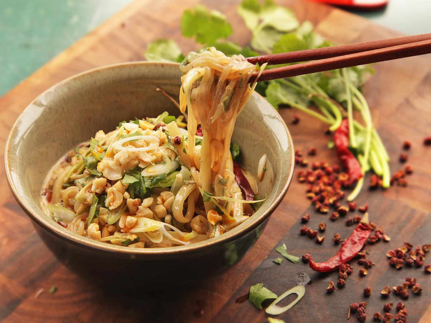 Using chopsticks to enjoy shiritaki noodles with chile oil, chopped chiles, scallions, and herbs alongside.