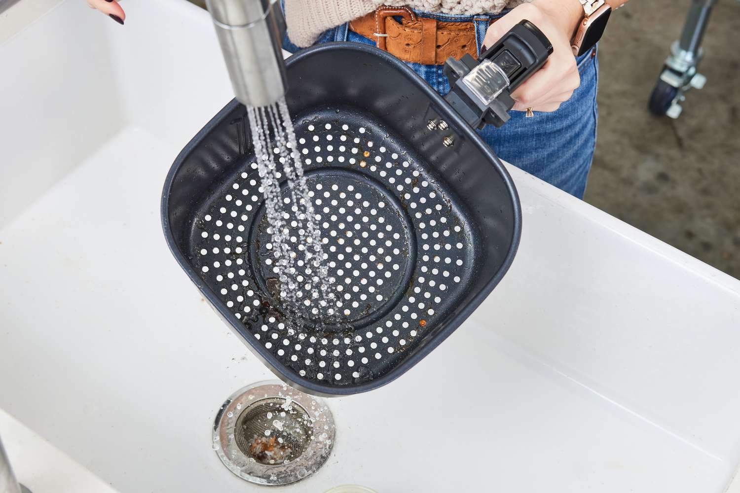 A person washing an air fryer basket in the sink.