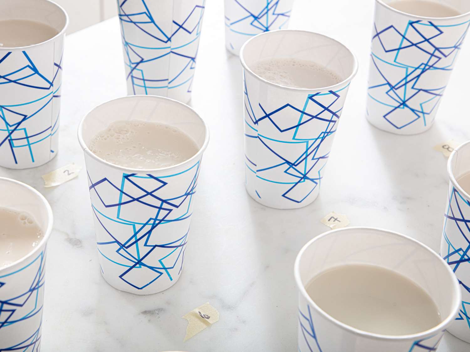 Several paper cups with abstract designs containing white liquid arranged on a table top with small markers