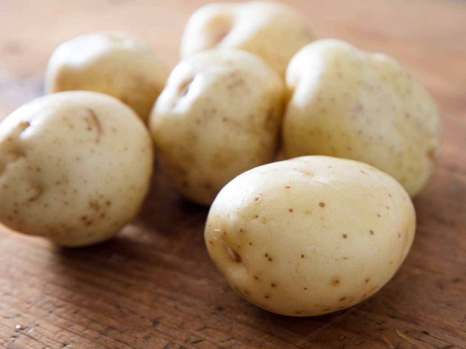 Closeup of a small pile of white potatoes on a wooden cutting board.