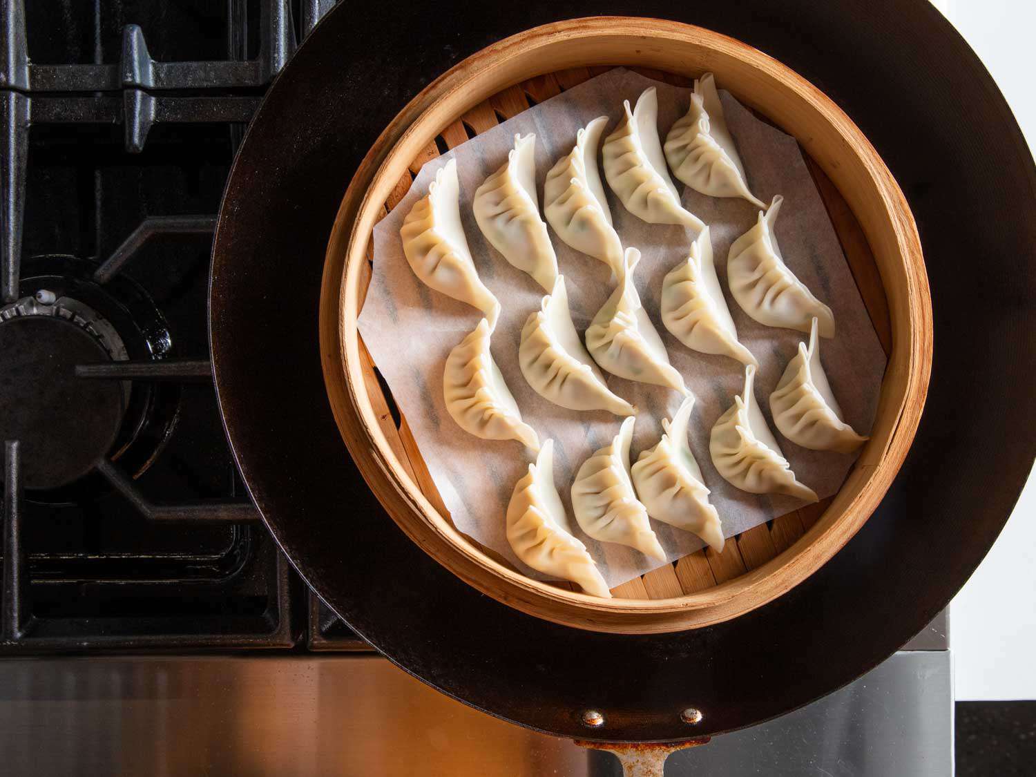 Overhead view of a bamboo steamer filled with dumplings set in a wok, ready to be steamed.