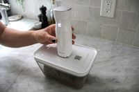 A hand holding a Zwilling Vacuum Sealer Pump on a food storage container on a countertop