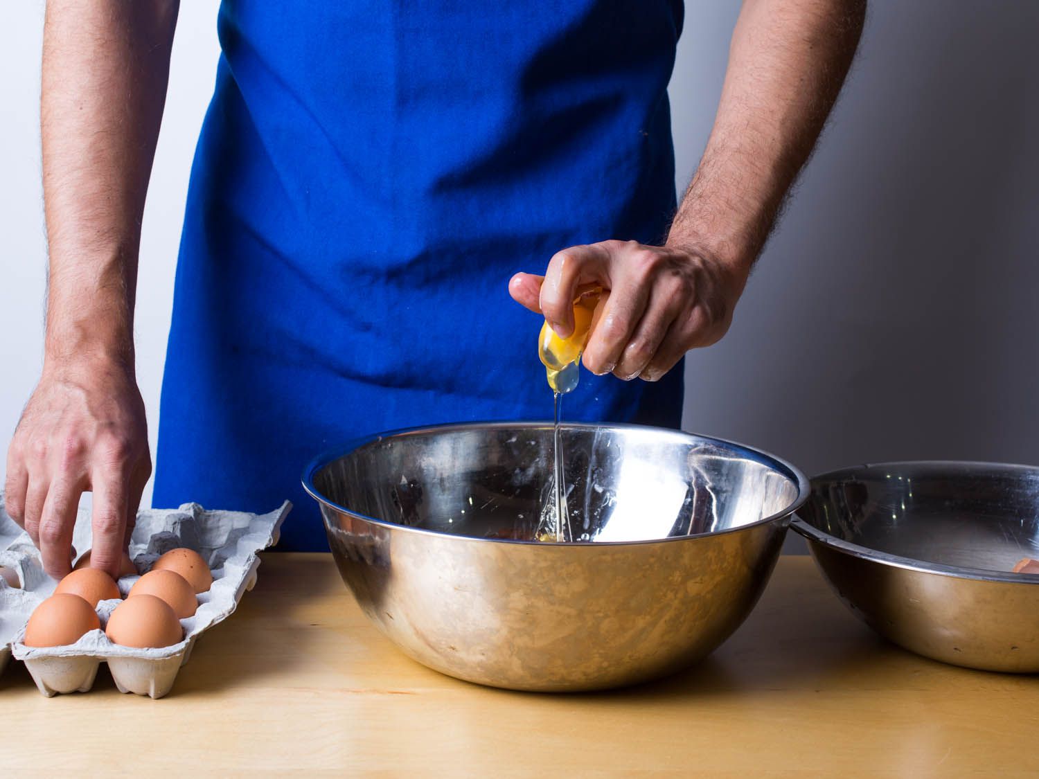 A person cracking egg with one hand into a metal bowl.
