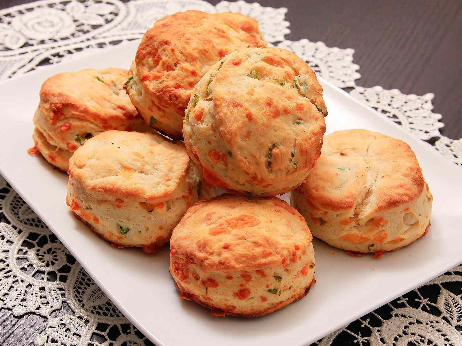 A white plate stacked with cheddar- and scallion-flecked buttermilk biscuits.