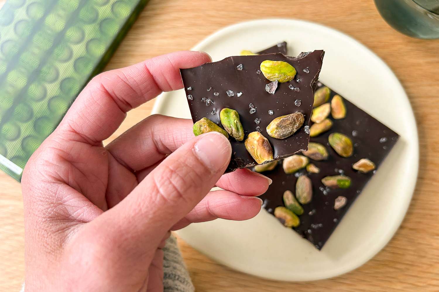 A hand holding a piece of Compartés Salted Pistachio Chocolate Bar