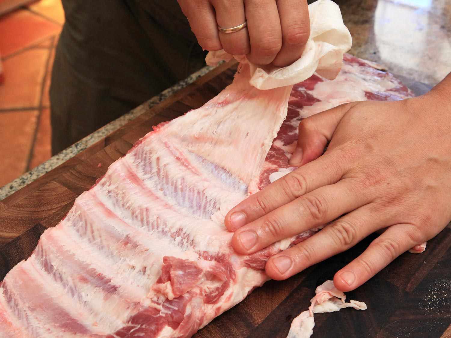 Two hands trimming uncooked pork ribs for sandwich.