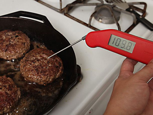 Author measures the internal temperature of the cooking burger patties with an instant-read thermometer.