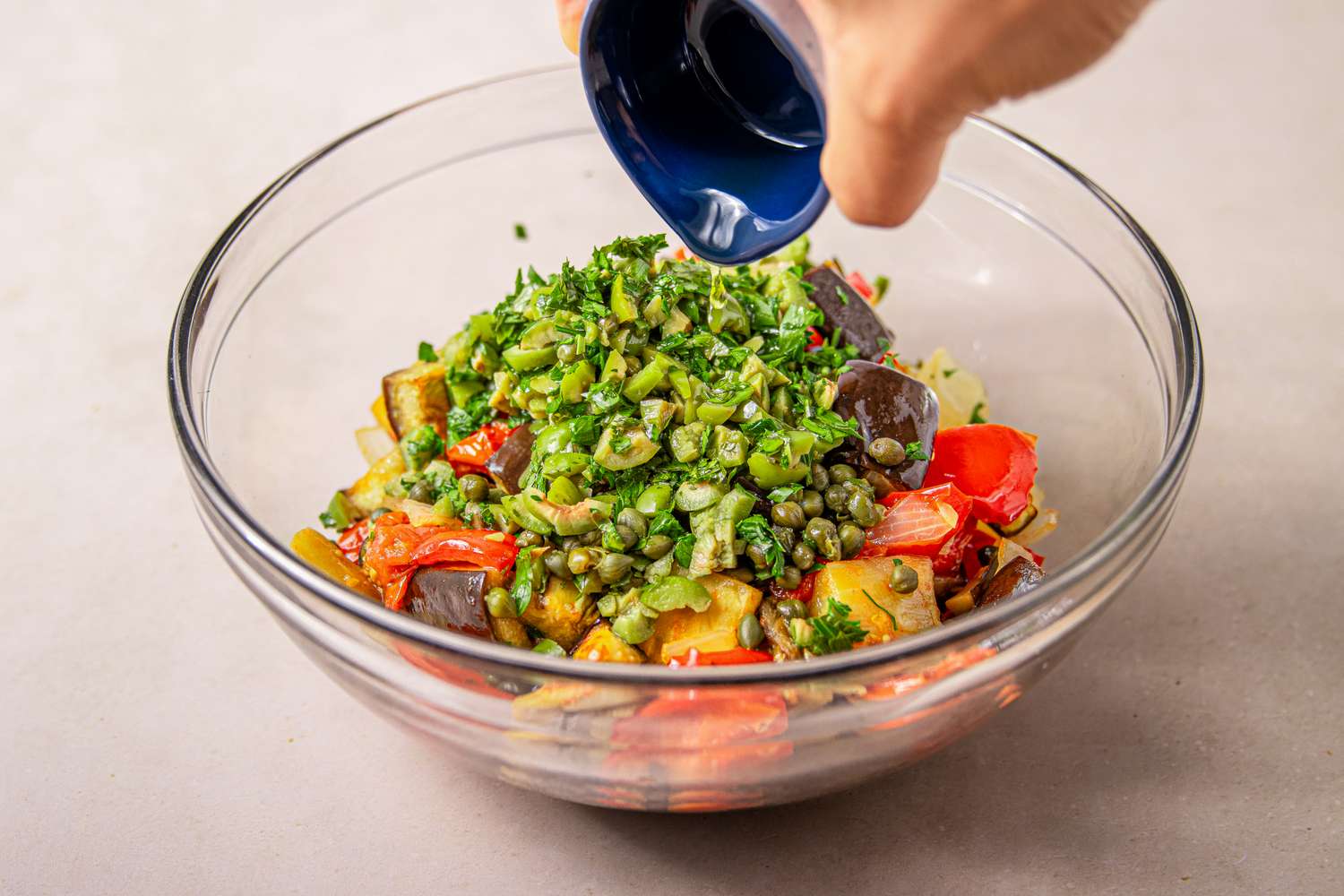 Glass bowl with vegetable caponata hand adding herbs from blue dish