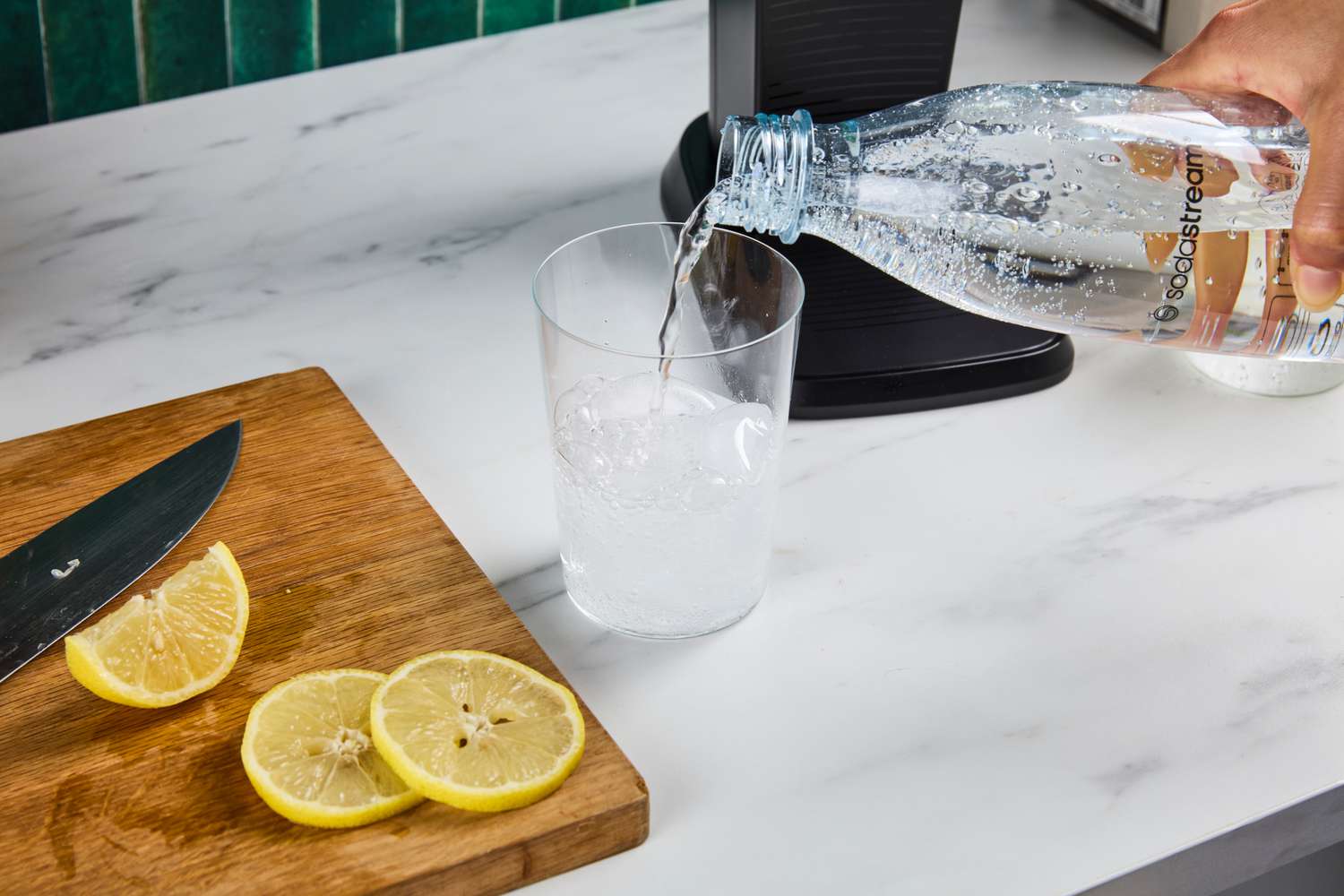 Water being poured into glass from a soda maker's bottle.