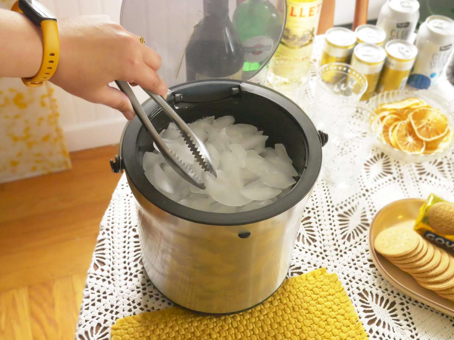 a person grabbing ice from the ice bucket at a table with tonic and glasses
