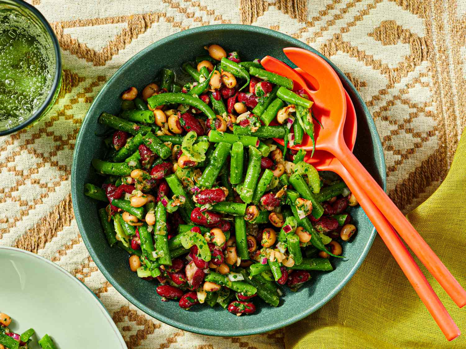Bowl of mixed bean salad with greens and utensils on a patterned tablecloth