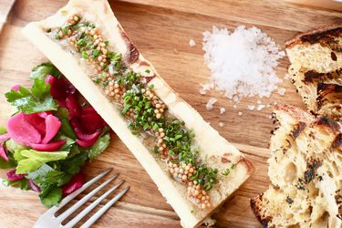 Roasted split bone marrow topped with a line of pickled mustard seeds served with fresh herbs, flakey sea salt, and grilled bread