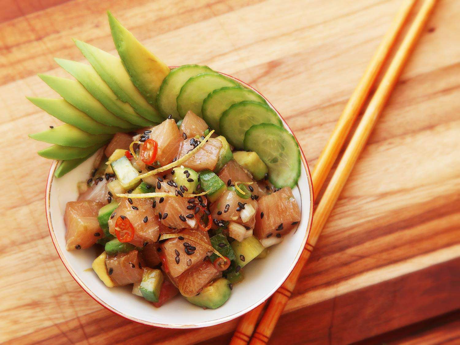 Overhead closeup of hamachi poke, garnished with fanned-out slices of cucumber and avocado.