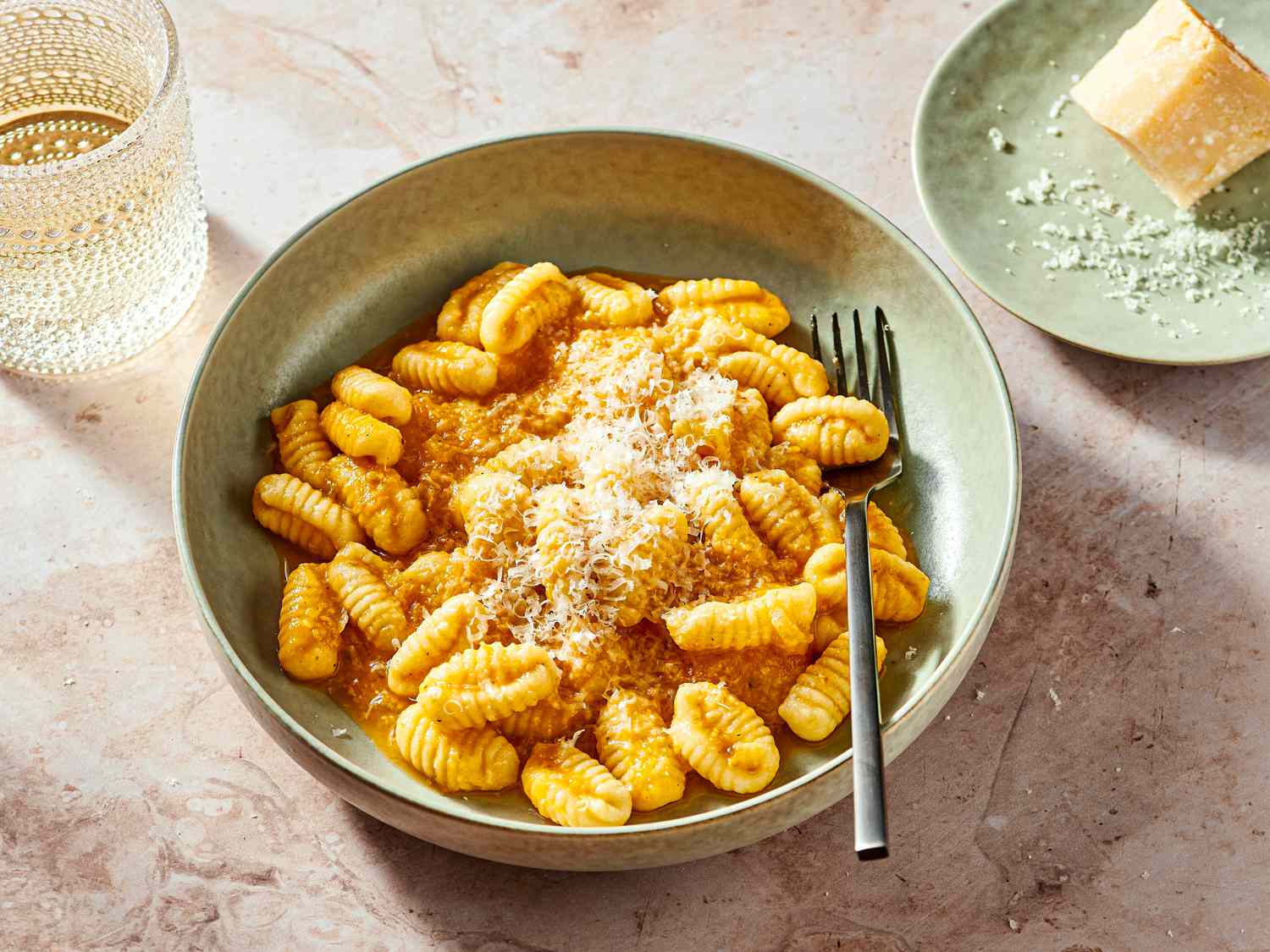  Fresh Cavatelli on a green bowl with a fork, with parmesan on a smaller green dish to the side, and a drink in a textured glass