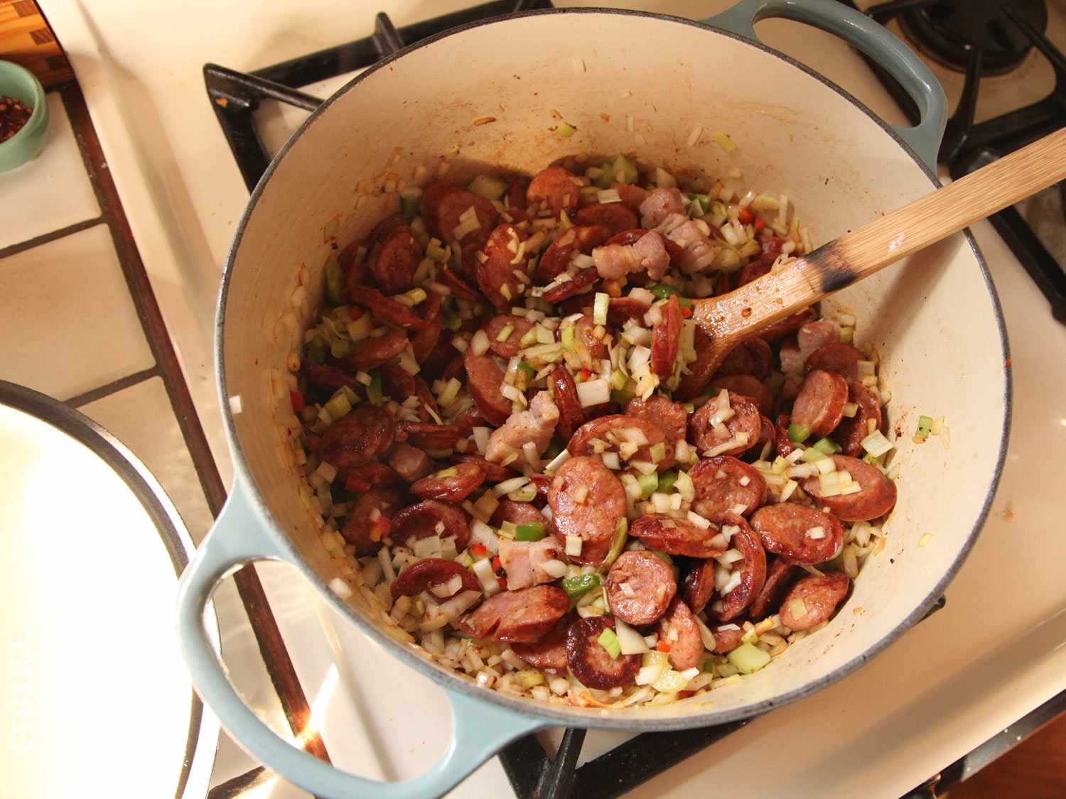 Andouille, pork belly, and chopped onions and aromatics are cooked in a Dutch oven.