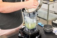 A person adding ice to a blender.