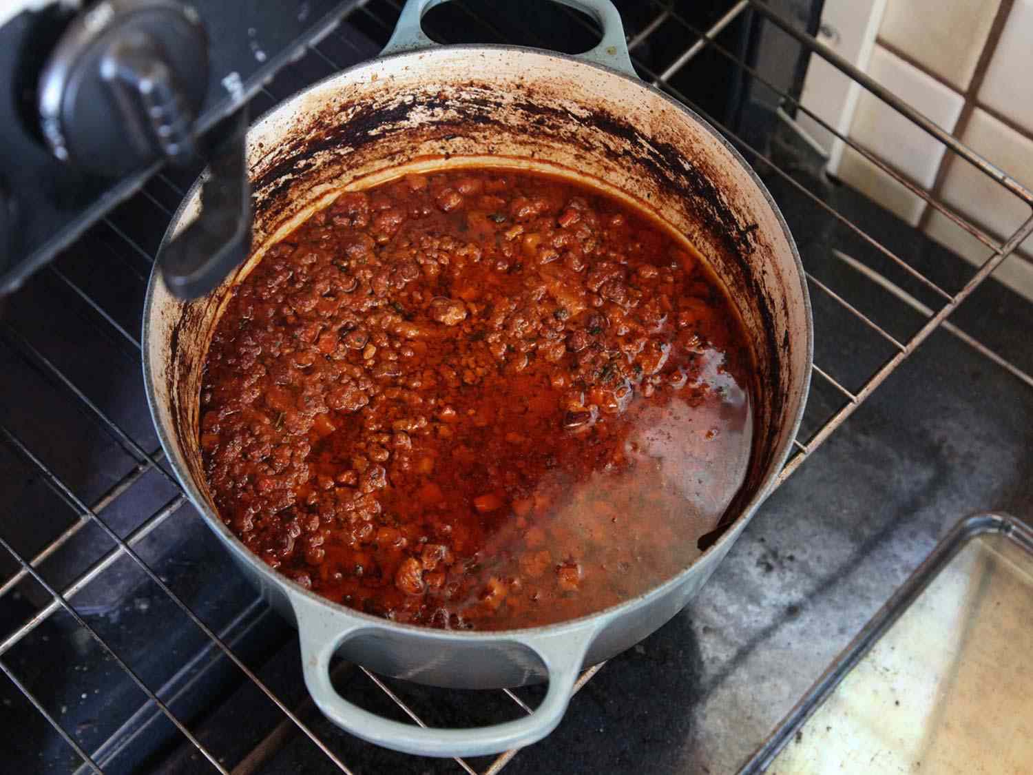 A meat sauce in a Dutch oven being placed in an oven.