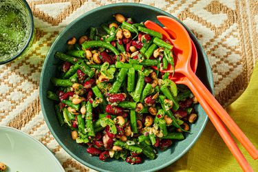 Bowl of mixed bean salad with greens and utensils on a patterned tablecloth