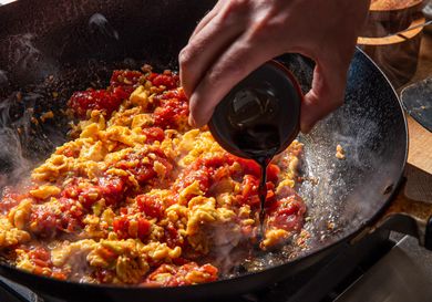 Ingredients being cooked in a pan with a liquid being poured in by hand
