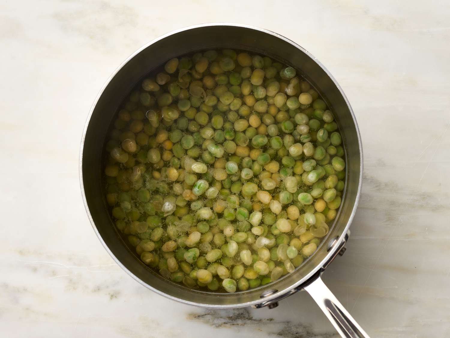 A saucepan filled with peas soaking in water on a marble surface