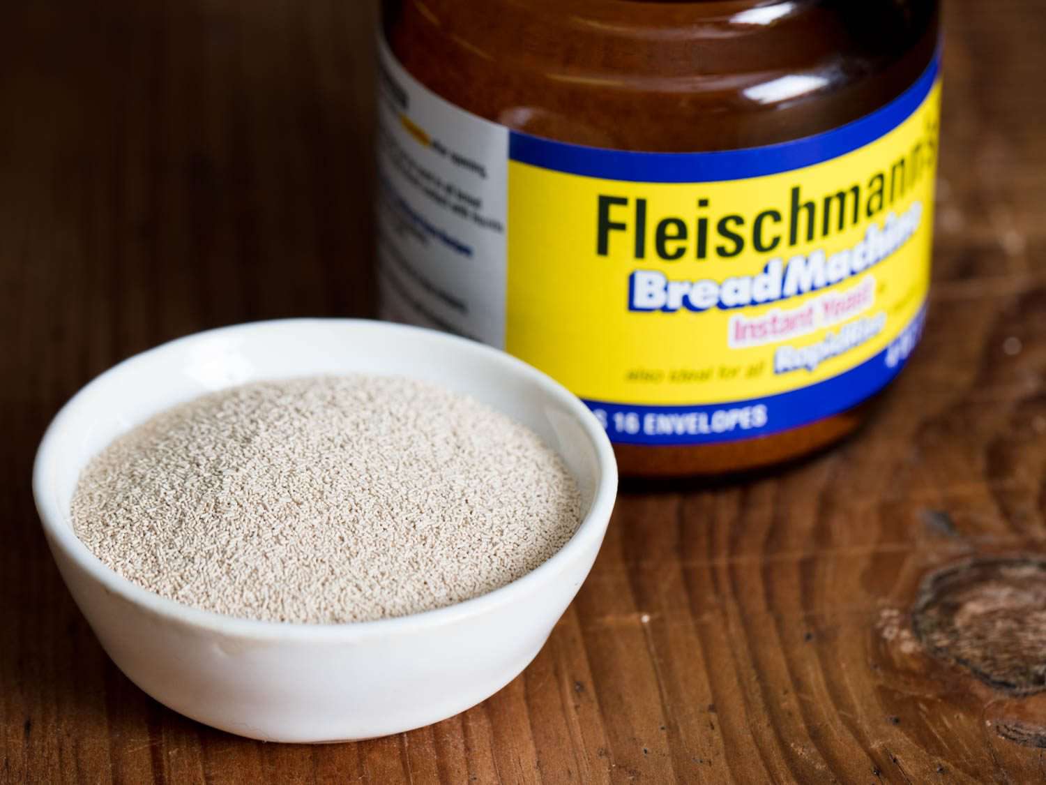 A glass container of Fleischmann's Bread Machine RapidRise Instant Yeast with some in a small white bowl