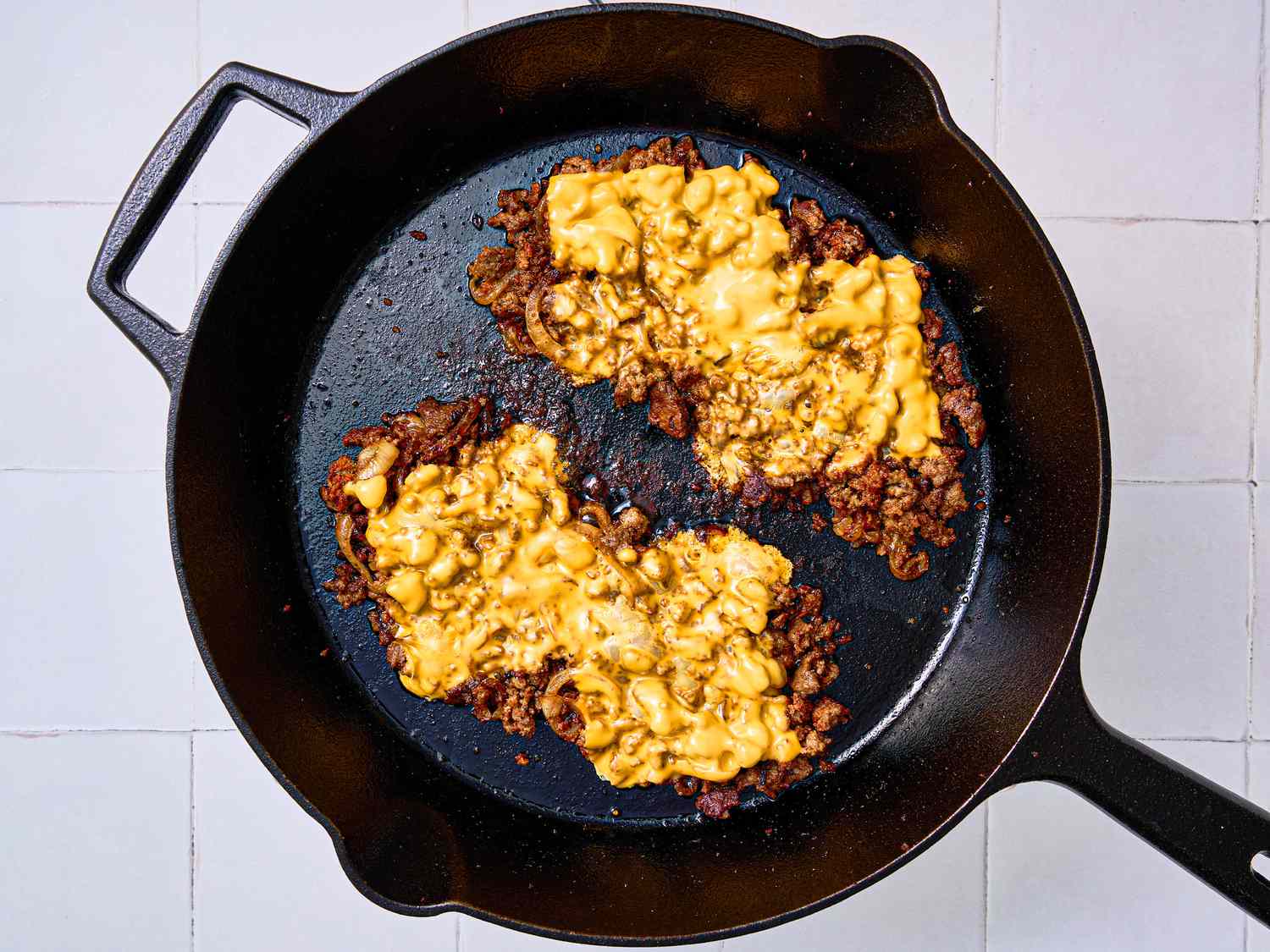 Cheese melting on top of ground beef in a cast iron skillet.