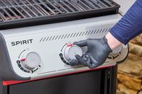 A gloved hand turning a nob on the Weber Spirit E-310 Gas Grill