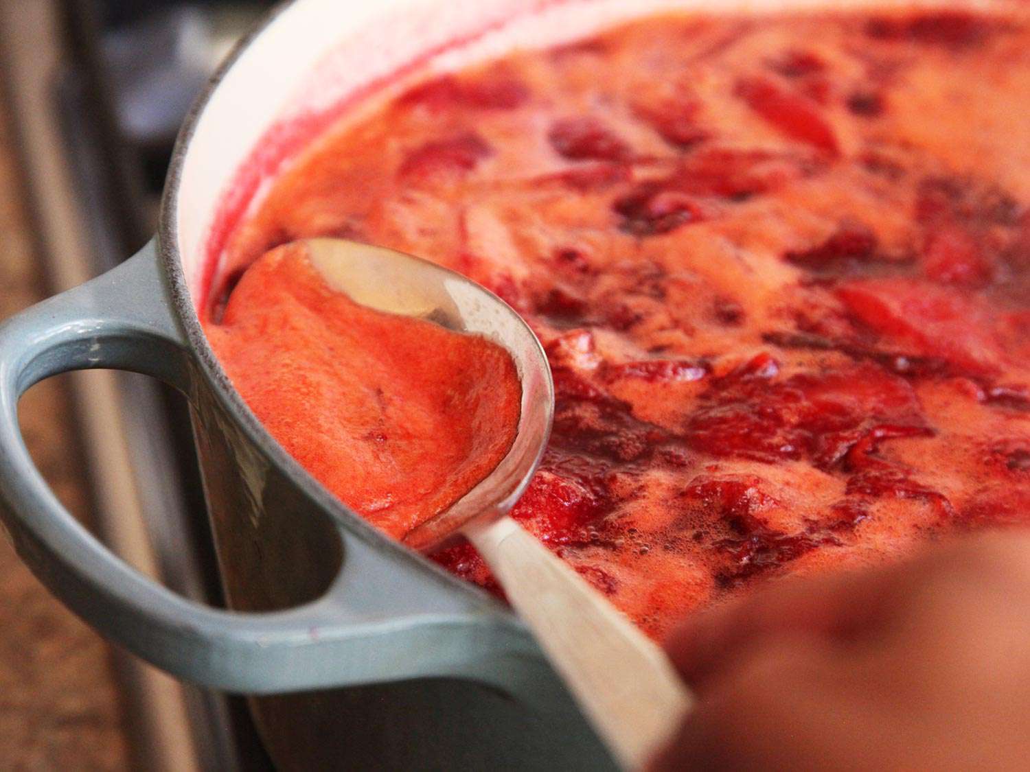 Foam is spooned from the surface of the simmering jam.