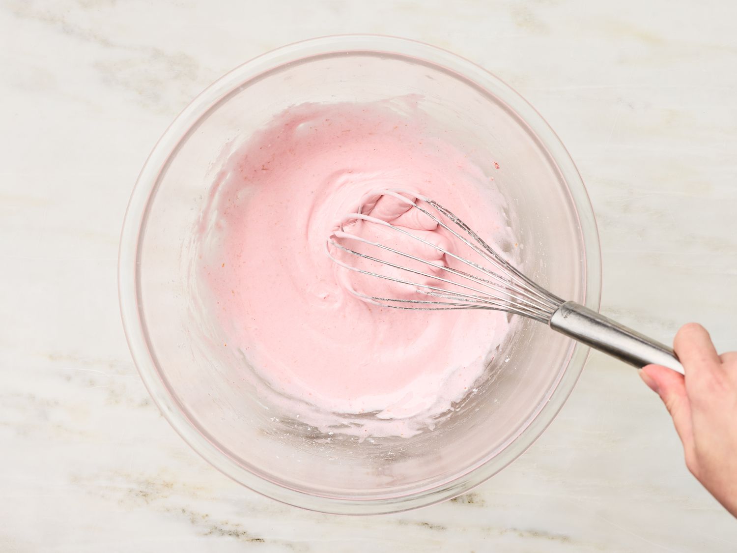 Hand whisking pink frosting in a glass bowl