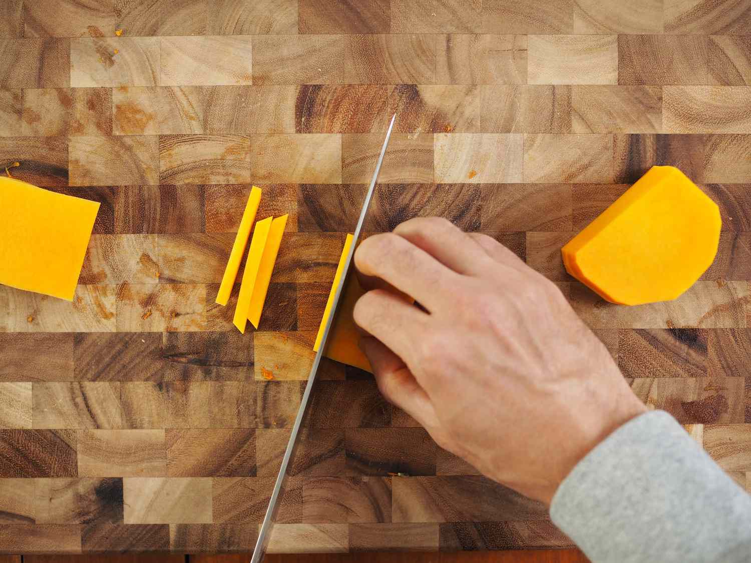 The thin planks of butternut squash being cut into thin strips.