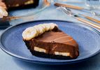 A slice of creamy chocolate banana pie on a blue plate topped with banana slices and a layered filling visible